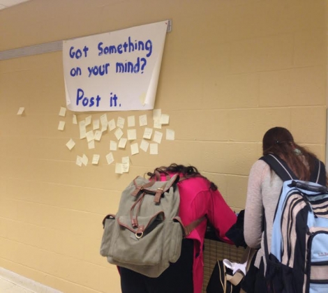 Two students jot down their thoughts on post-its as they pass through the art hallway. (photo by claire boenitz)