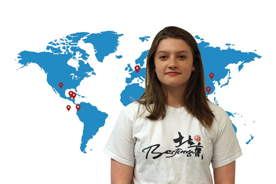 Junior Aslee Addison poses in front of a map with pinpoints of several places she’s visited around the world. With Addison regularly traveling, she has become familiar with the countries and think of it as a “home away from home.”