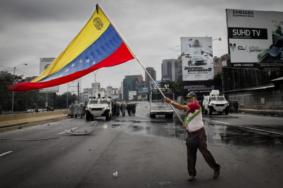 CARACAS%2C+VENEZUELA+-+MAY+3%2C+2017%3A+Protest+in+Caracas%2C+Venezuela.+Deputy+of+the+National+Assembly+holds+a+Venezuelan+flag+when+the+protest+is+repressed+by+the+Bolivarian+National+Guard+with+tear+gas.+-+Image%0A