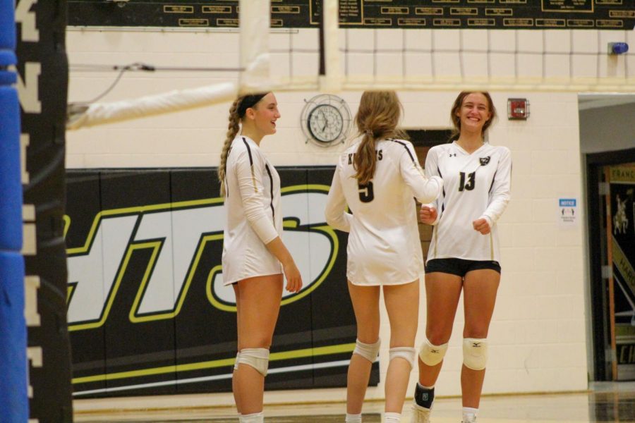 Three varsity volleyball players laugh during a volleyball game. Brianna Wortman did not play in this game but supported her team from the sidelines.