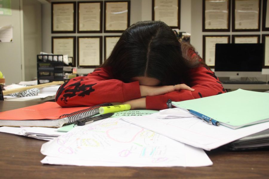 In the publications classroom, Junior Chloe Ellison lays down stressed on a pile of homework. Ellison has a lot of homework which causes a great amount of stress.