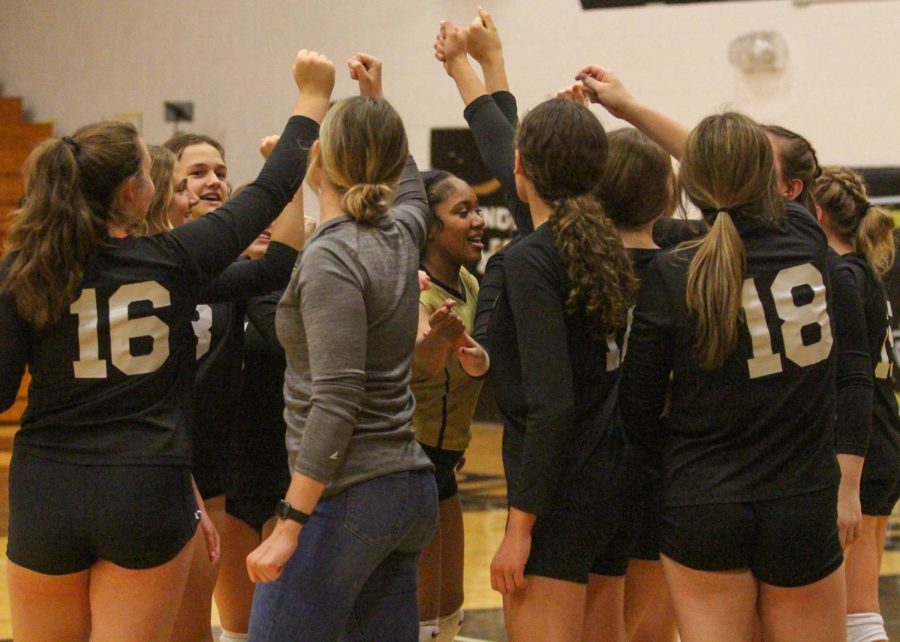 The varsity girls volleyball team huddles together at a game.