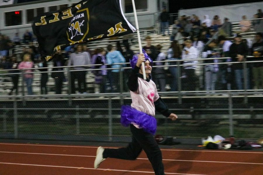 A senior runs across the track at the Francis Howell Central carrying a Francis Howell North flag during the 2021 Powder Puff