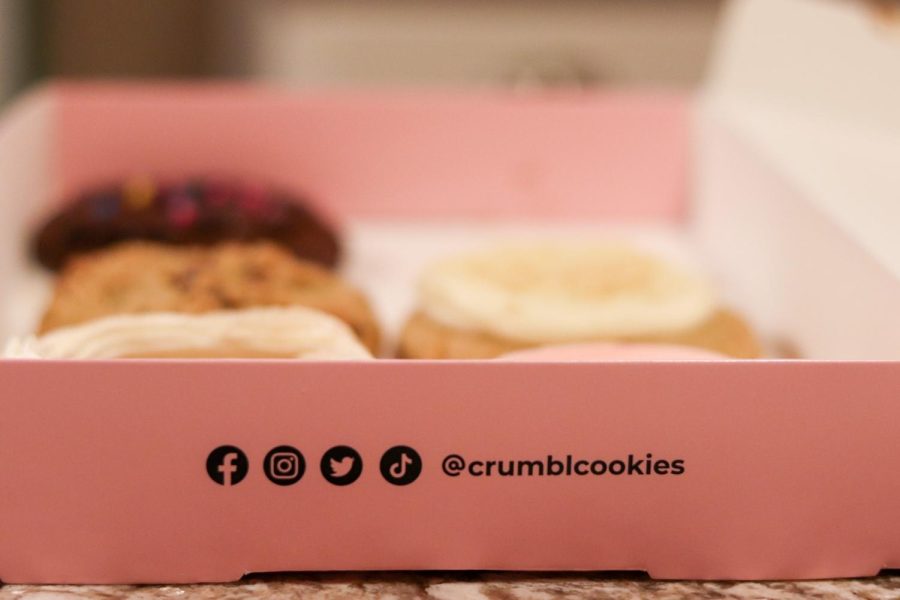 An open box of Crumbl Cookies sits on a kitchen counter. Crumbl Cookies is a cookie shop created by two cousins and first opening in Logan Utah in 2017. Crumbl implements a rotating menu, meaning that each week will have new cookies.