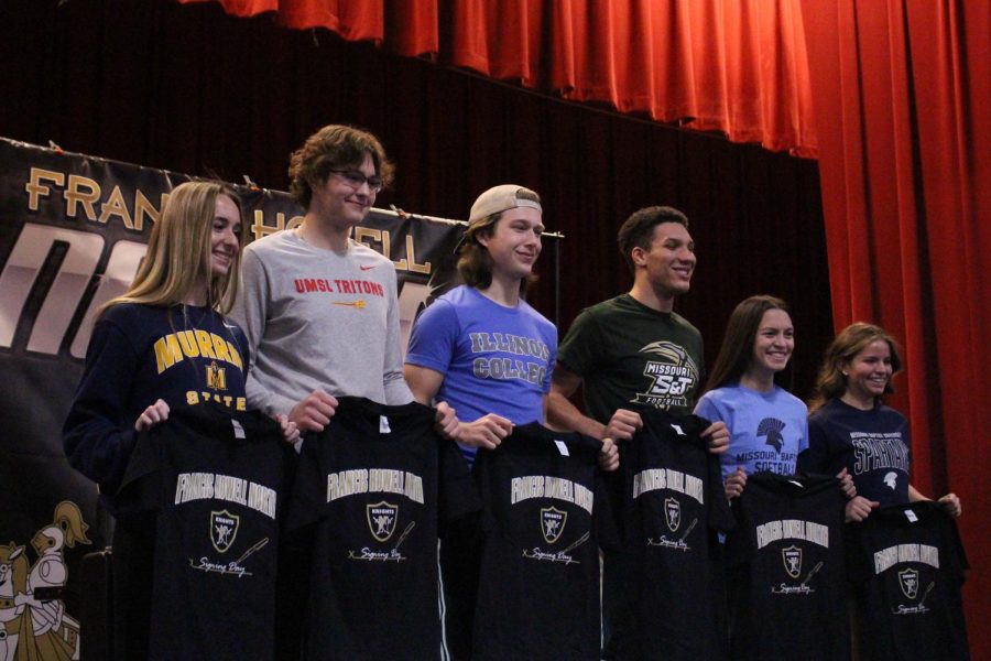 Seniors Sami Wilson, Trey Scneider, Jordan Minter, Ian Kelly, Lucy Fajatin and Anna Rose Eldred stand together in the auditorium holding shirts they received during the College Signing day ceremony