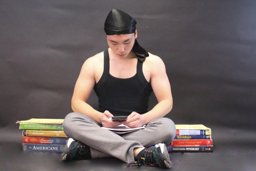 Senior Pacino Lin sits surrounded by textbooks and papers while working on his phone.  