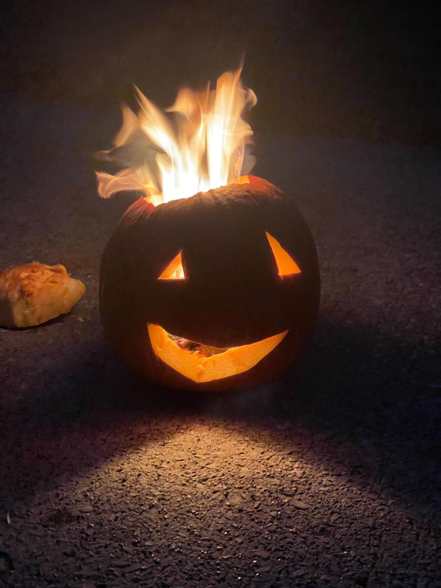 A carved Jack-o-lantern is set on fire in the street.