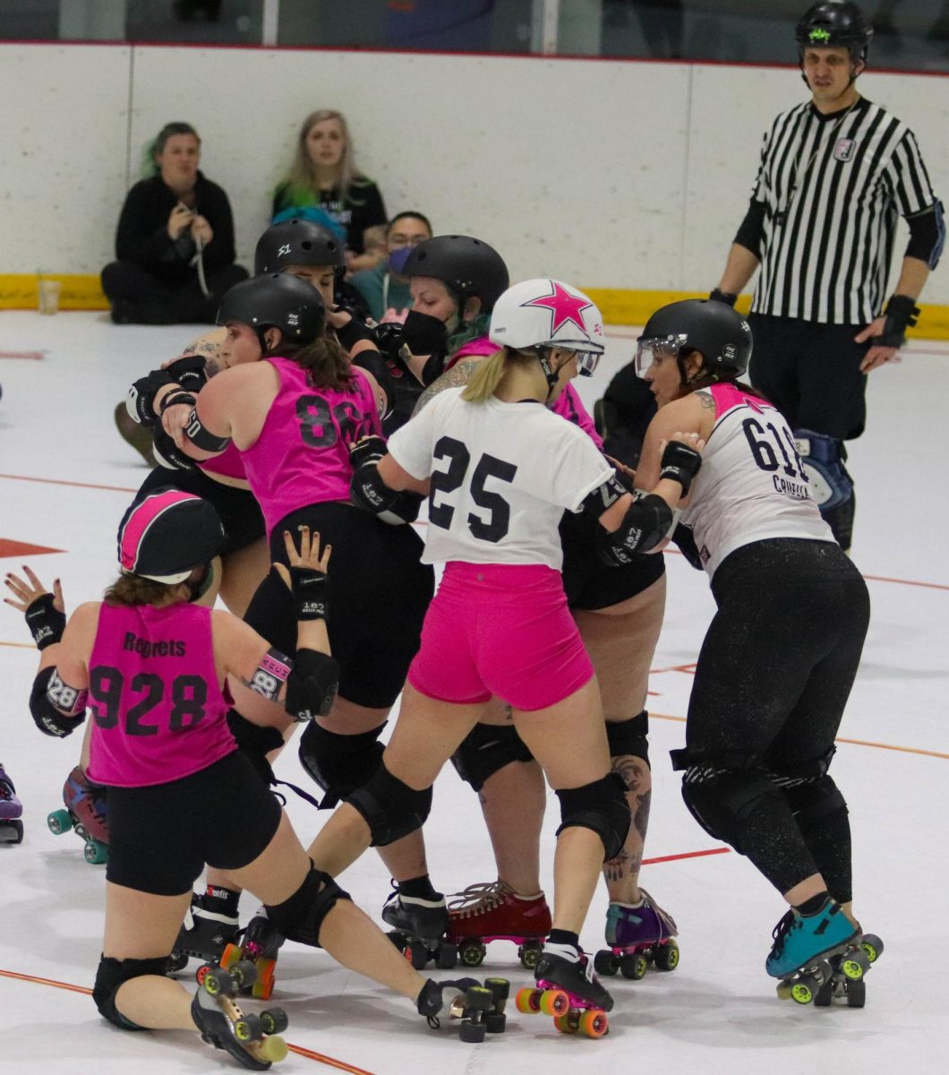 The jammer on the white team, number 25, attempts to get through the pack as the pink teams pivot, number 928, holds her hands up in the air during the final scrimmage on the night of Feb. 17. There are red lines around the track that players are not allowed to go in or outside of, which is why 928 is holding up her hands, as anyone outside of the track cannot interact with those inside. Players who skate off of the track have to skate outside and reenter at the back of the pack.

[Roller derby] is football on skates with no ball, junior derby player Abbie Wann said.
Well, its kind of like that, but it’s not that hard, junior derby player Maeko King said.
