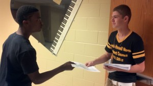 StuCo representative hands out fliers to students at meeting.