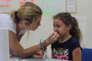 Sophomore Abby Day paints a little girls face at the Harvest Ridge carnival. 