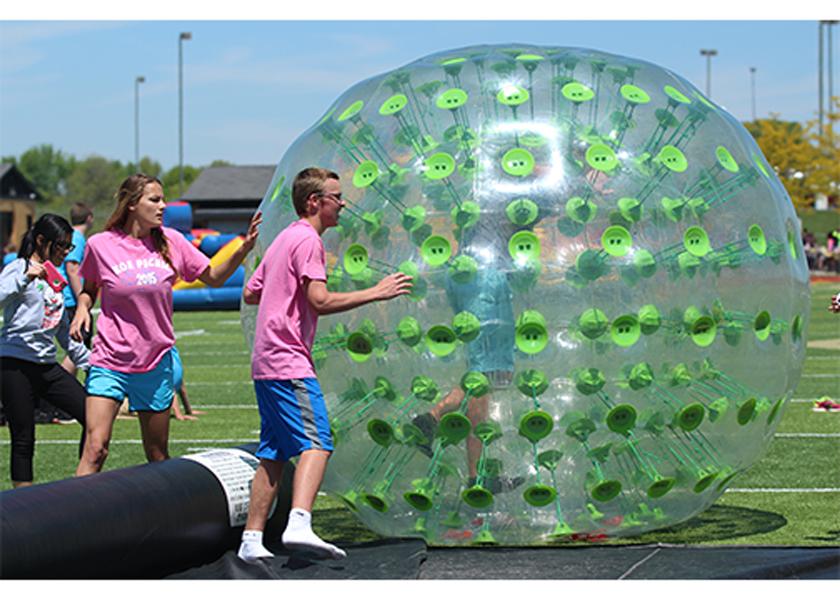 Junior KOE members Jessica Jones and Drew Lanig help students get into an inflatable ball, in which they raced down the field in. The picnic is a yearly reward with food and games, for students with good grades, being student of the week or having good attendance.  (File Photo)