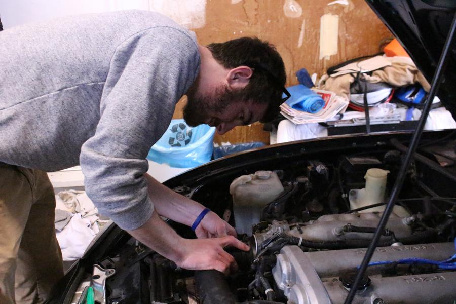 Putting the end tank hose back on the throttle after cleaning it, he uses the same socket to tighten as he used to loosen the bolt. He makes sure that he tightens the pipe but not too tight because he does not want to bend the clamp.