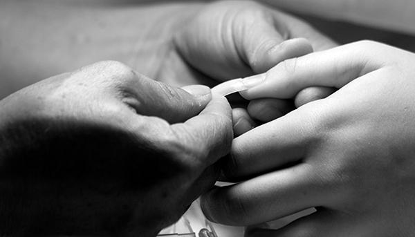 The nail salon worker puts the nails on Browns fingers. This is the very first step into getting fake nails. The salon worker starts to put the plastic tips on for the length of the nails.