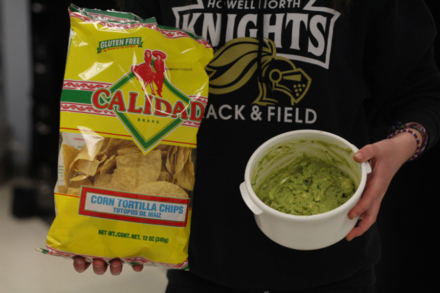 The completed guacamole is held next to a bag of tortilla chips.