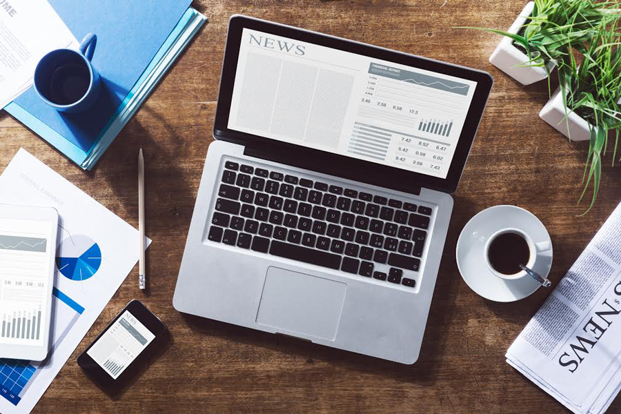 A laptop sits on a table, surrounded by different newspapers and a cup of tea. (Source: Shutterstock/Stokkete)