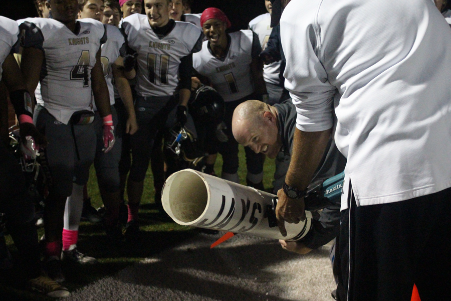 Coach Mike Bevill cuts the pipe, while head coach Brett Bevill holds it in place, after the Knights defeat Washington High School 41-25.