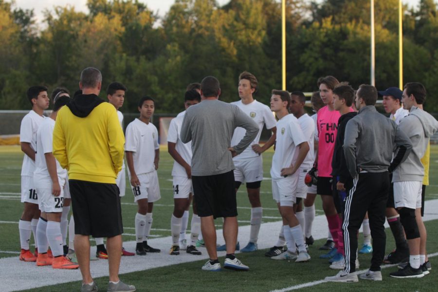 Coaches Larry Scheller [in yellow] and Zach Fettig talk to the soccer team before playing against CBC