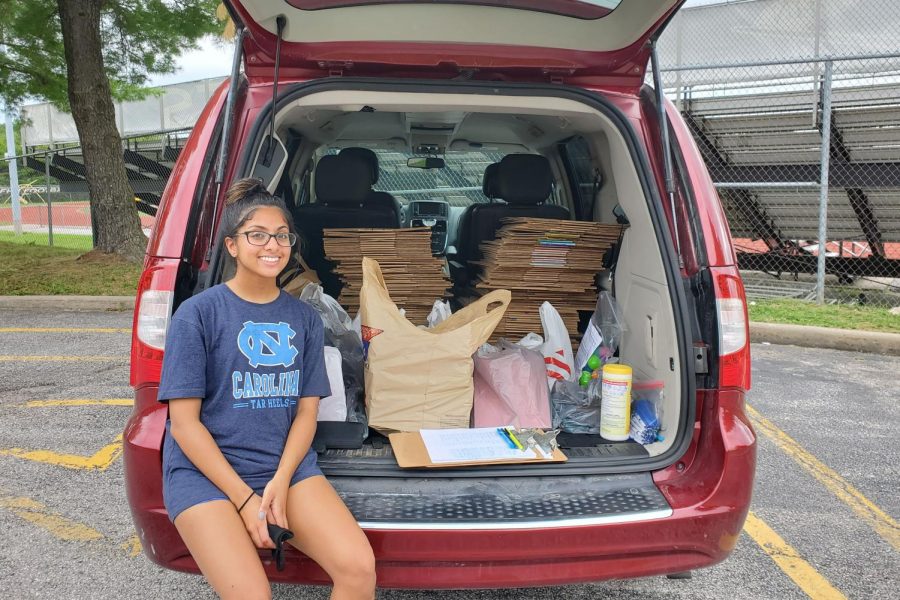 Senior Riya Contractor sits in the back of a car with care packages for charity.