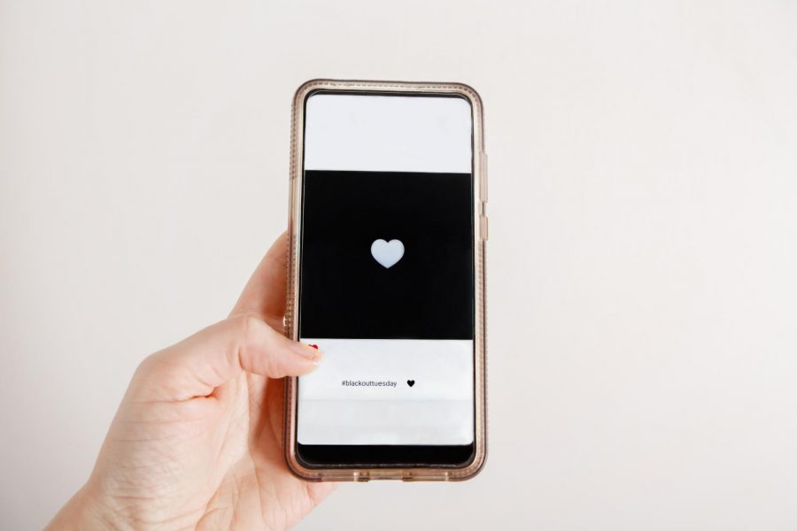 A phone is held up, with a social media application open showing a black screen. "Black-Out Tuesday" was an event over the summer where students posted black squares to show respect for the Black Lives Matter movement.