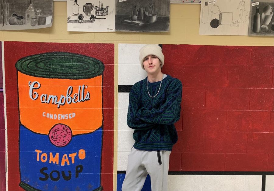 Connor Buschmann stands next to murals in the art hallway. He has a passion for art and hopes to grow his skills in street art and spray paint.