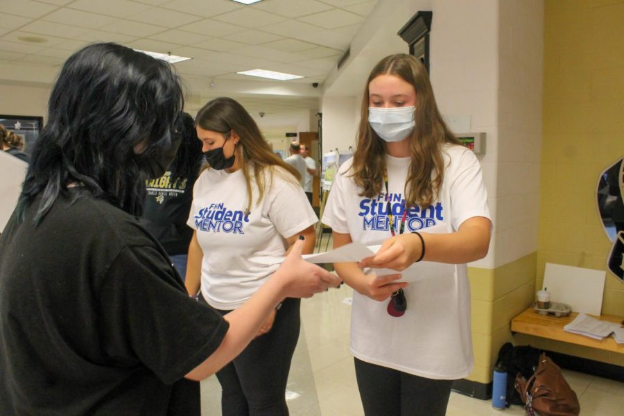 Junior Isabella Volmar hands an incoming freshman a paper itinerary for the day. 