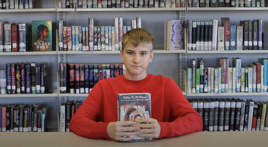 Hunter Van Dyne sits at a table holding a book titles 'One of us is lying'