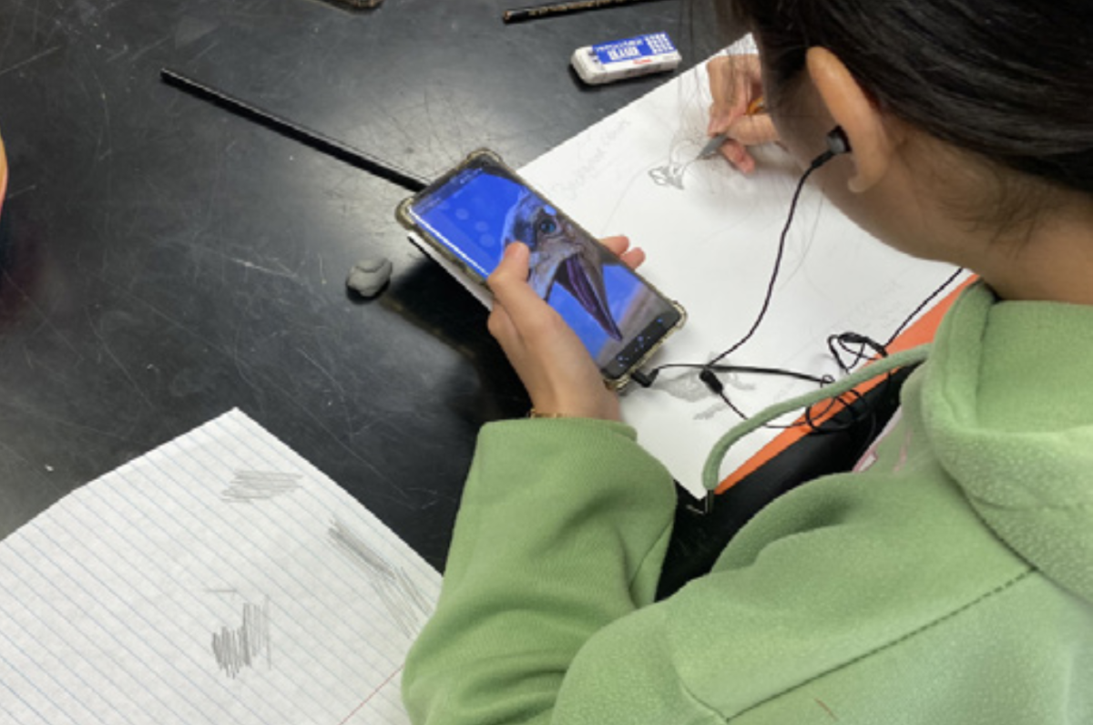 Martha Sacay works on an art project while using her phone for a reference. 