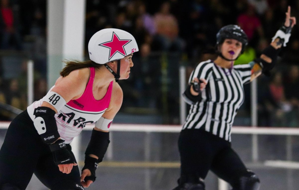 Number 48 on the white team looks ahead as she skates around the track during a scrimmage on Feb. 17. A ref holds up their arm in the background, signaling the skater as the lead jammer. The lead jammer in a given jam is the first player with a star on their helmet to break through the large group of blockers, also known as the pack. Being signified as lead jammer gives that player the ability to end the jam at any time by tapping their hips.

"I was a skater for seven years," outside pack referee Kim Mason said. "I started playing in 2012 and I had heard about it for years before that. My job tonight was to watch the skaters from the outside of the track and watch for penalties."
