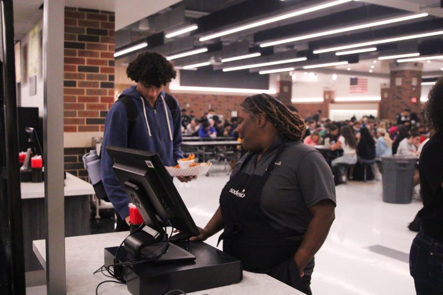 A cafeteria aid assists a student in checking out for lunch. 