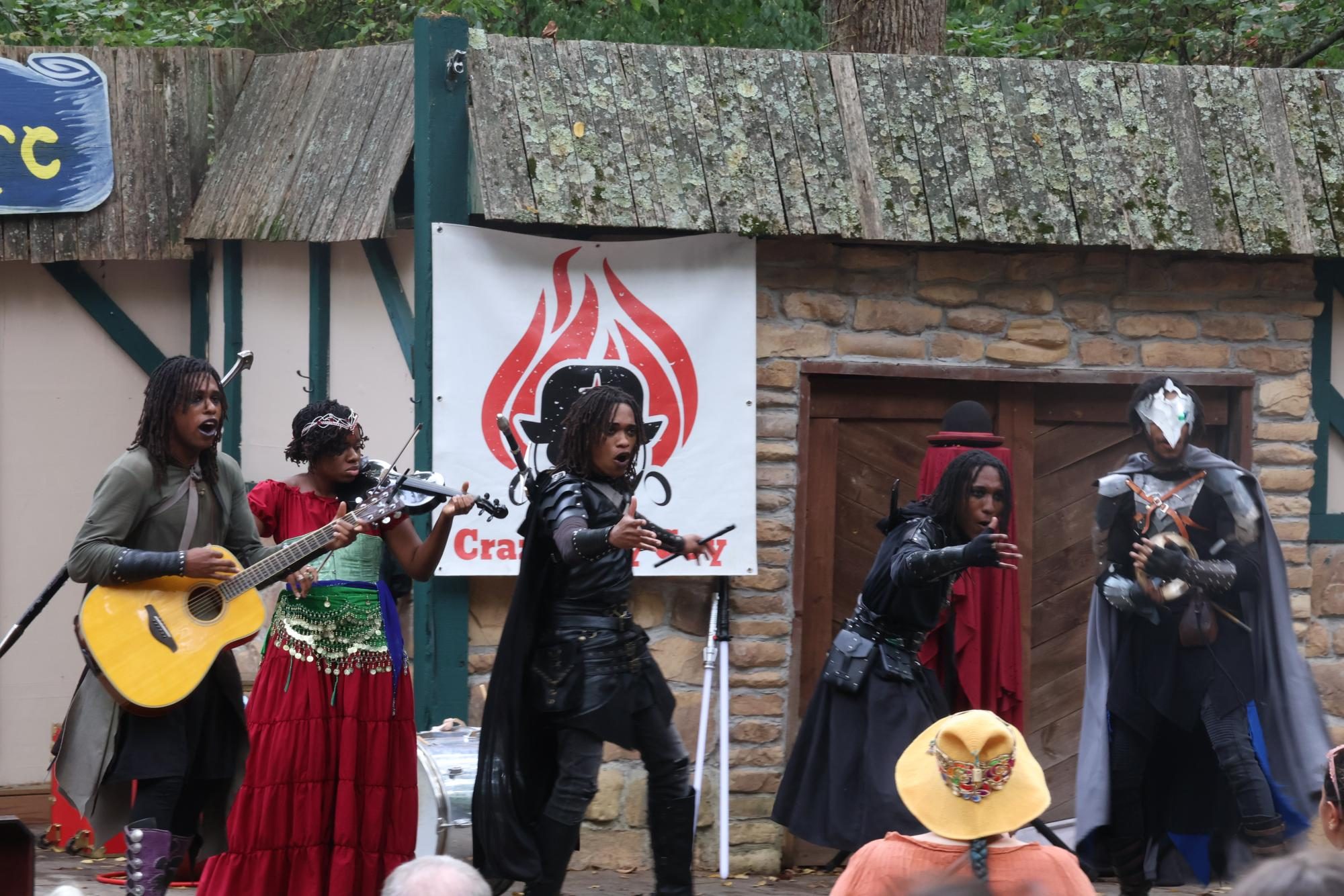 A group of performers come together in front of a crowd. Some play instruments while others start a chant with the crowd. 