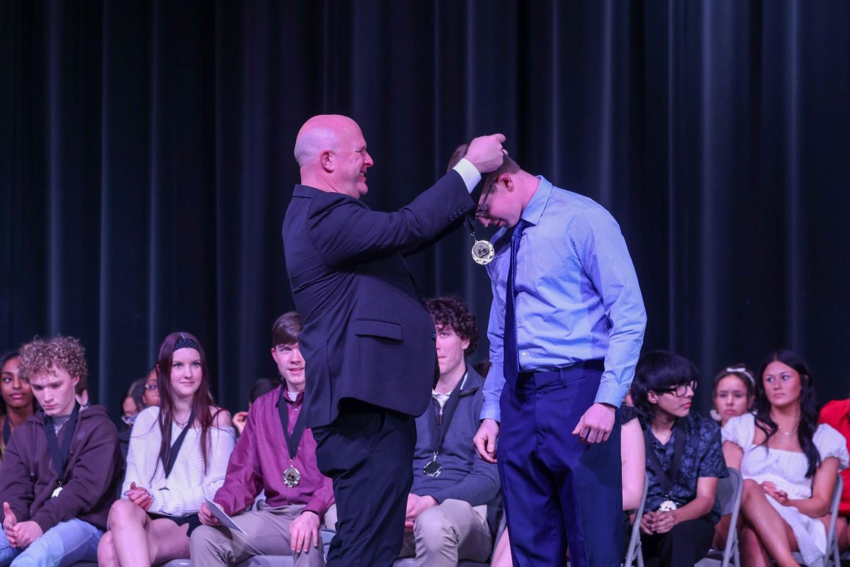 Principal Jon Shultz awards Knights of the Round Table medal to student. 