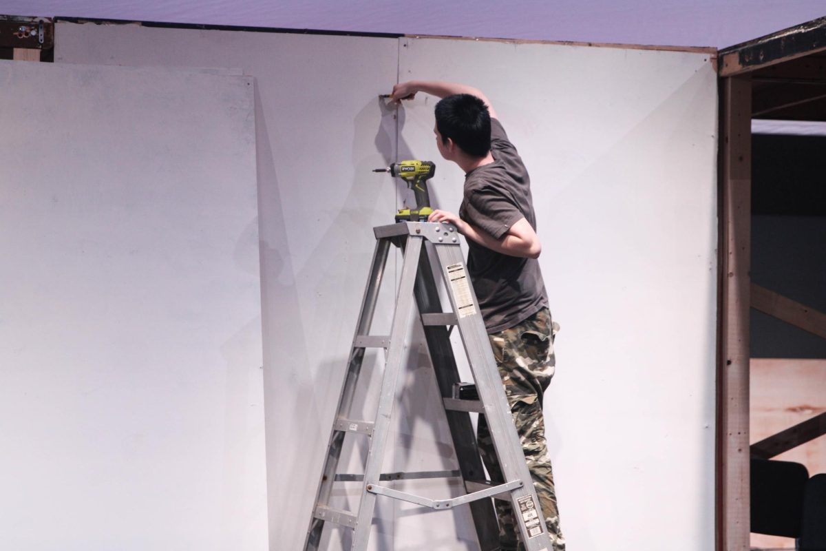 Senior Victor Balleydier works on the set on stage while the ensemble rehearses choreography on Wednesday, Jan. 27. Typically, set pieces and structures are assembled in the scene shop, then moved out on stage to be secured with the rest of the set.